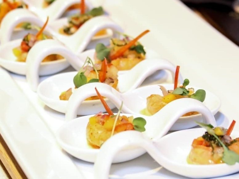 A row of canapé spoons plated with saffron and micro herbs