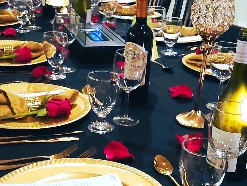 A dining table dressed with gold chargers, roses and wine for a private dinner