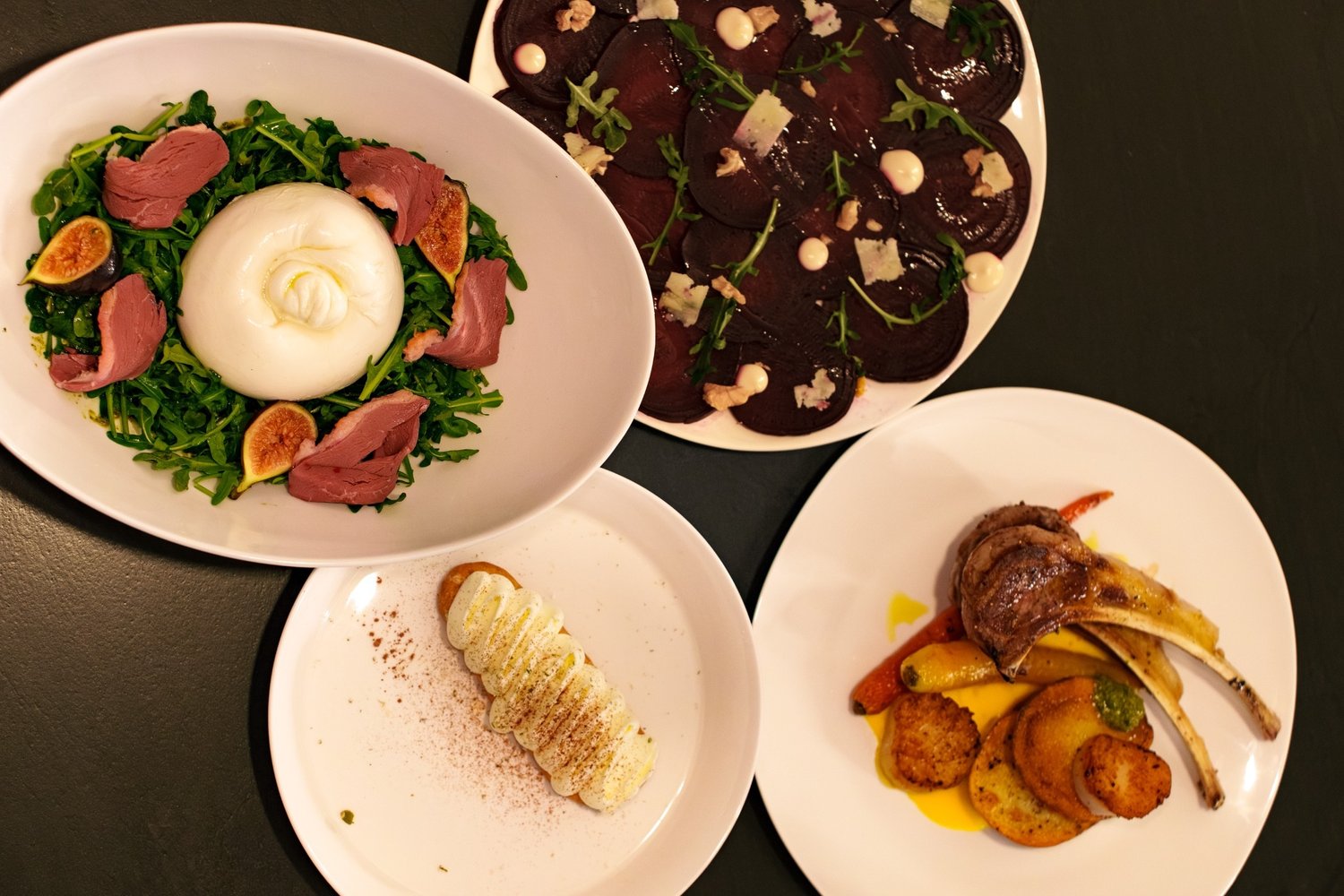 Four plated courses laid out together on a dark table