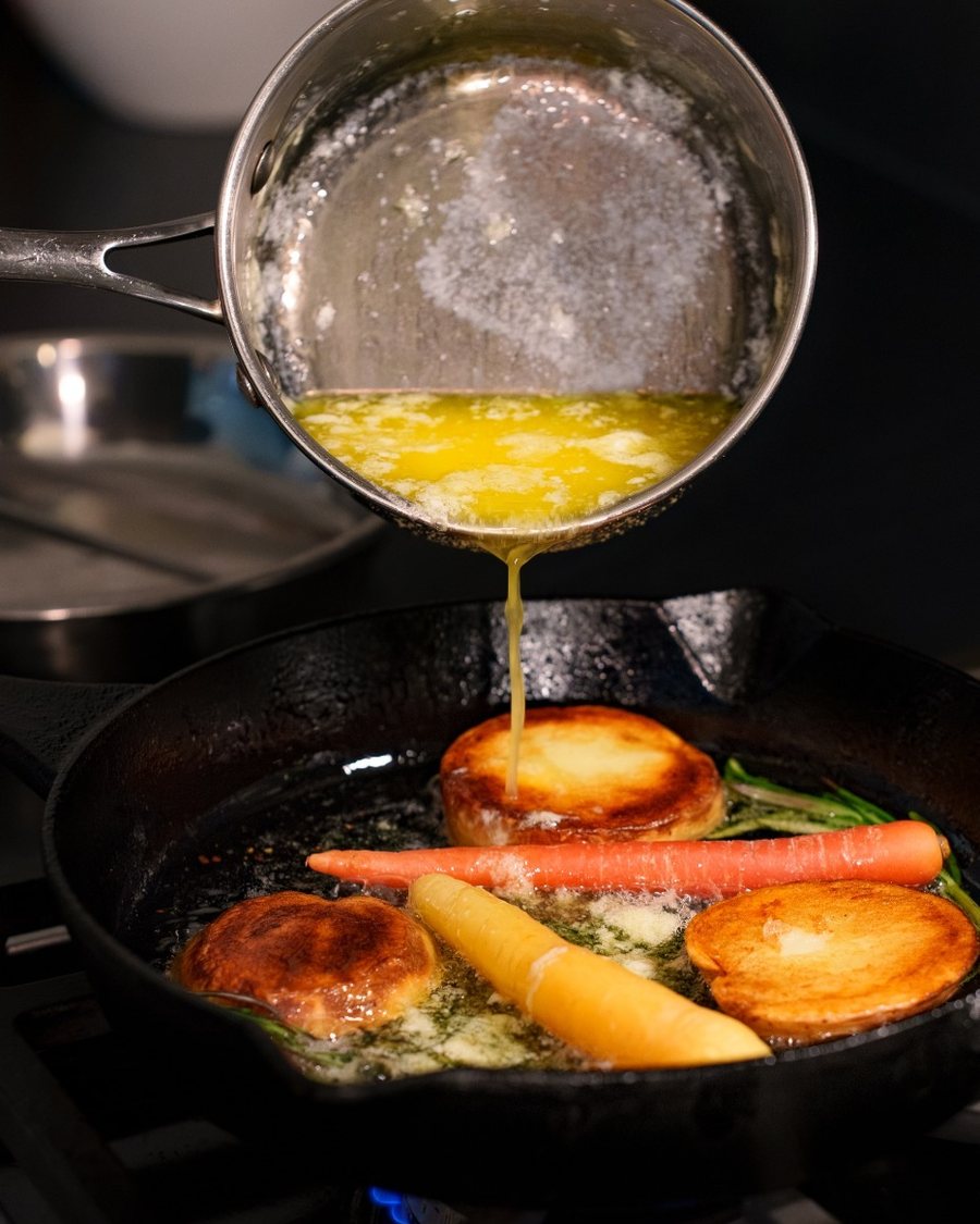 Butter poured over carrots and potatoes in a cast-iron pan on the burner