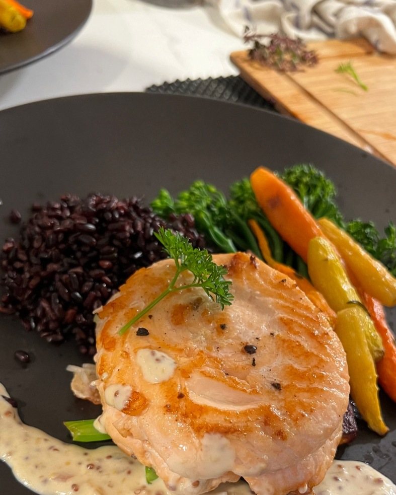 Pan-seared salmon on black rice with a cream sauce and baby vegetables